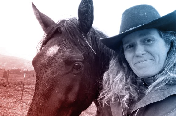 A woman wearing a cowboy hat with a black horse.