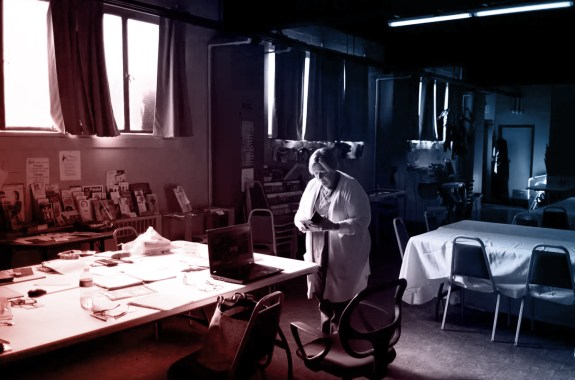 A woman standing in a darkened room reads a small book.