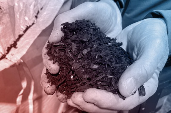 A pair of hands holding a pile of black dirt-looking stuff.