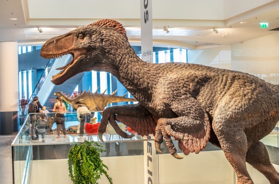 A large beige statue of a fearsome dinosaur with feathers covering its body, walking on two legs