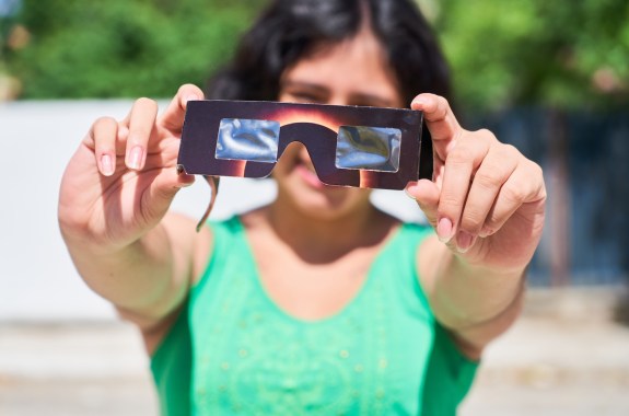 Happy young latina woman with solar eclipse glasses, watching a solar eclipse