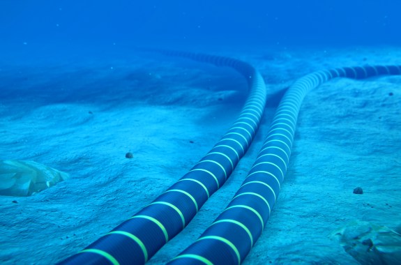 Two thick black cables extend out across the ocean floor, in a bright blue underwater view.