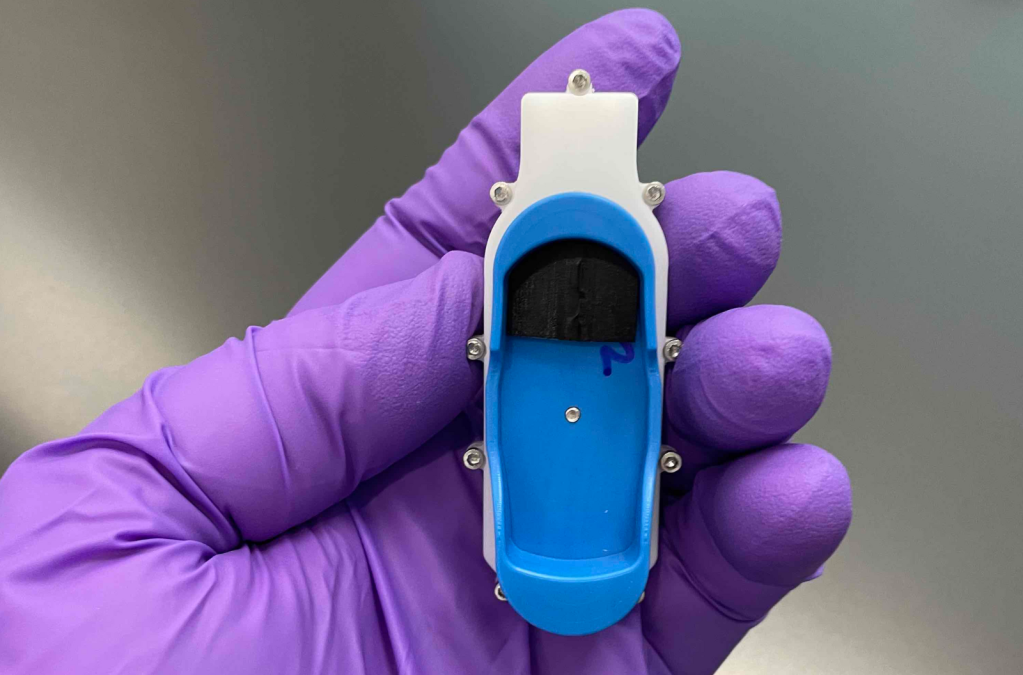 A purple-gloved hand holding a device the size of a thumb.