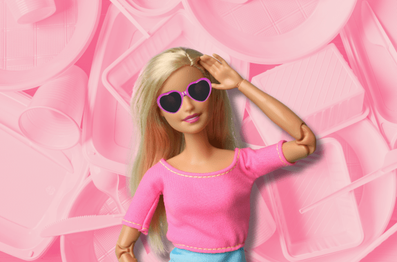 A Barbie doll wears sunglasses as she stands in front of a backdrop of pink plastic containers.