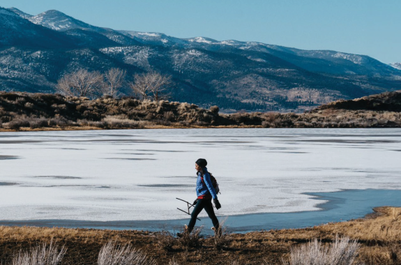 A woman dressed in winter gear walking across a beautiful tundra landscape.