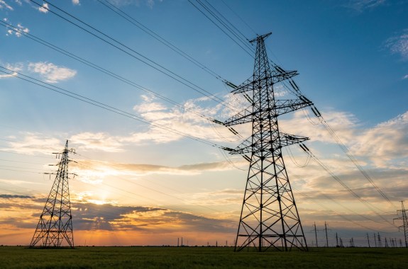 silhouette of high voltage power lines against a colorful sky at sunrise or sunset.