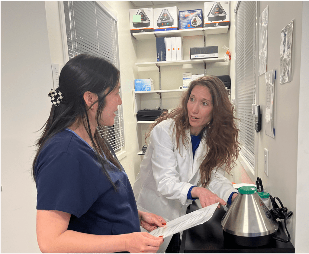 Two women speaking to one another, one wearing a lab coat and one wearing scrubs.
