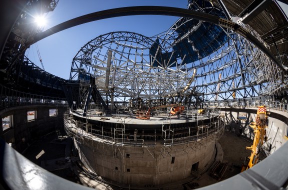 Looking up through a dome of scaffolding and construction cranes at blue sky