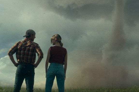 Two people looking at a tornado on the horizon of a landscape