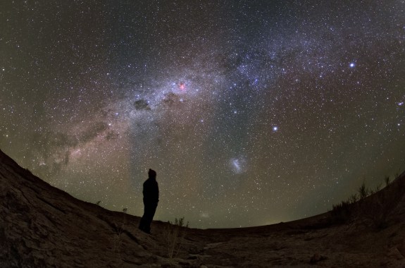 The silhouette of a person staring up at the milky way from a barren, rocky landscape