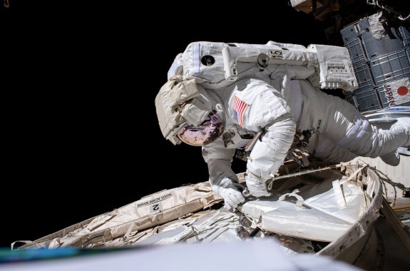 An astronaut wearing a space suit is on the outside of the ISS working on its exterior