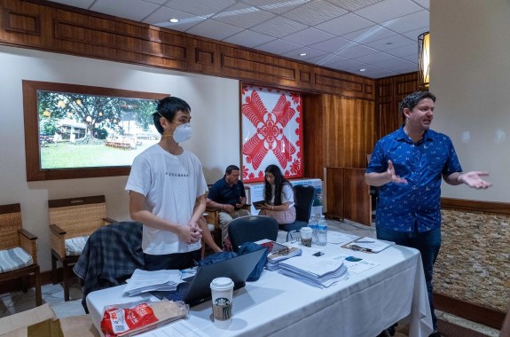 Two people standing at a table speaking.