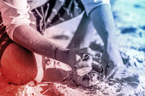 A man skewers a fish with a hook on a sandy beach