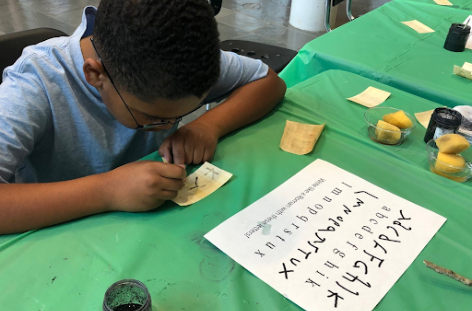 A young child writes on papyrus paper with dark ink.