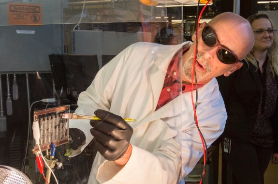 A man wearing sunglasses paints a clear fluid onto a glass panel