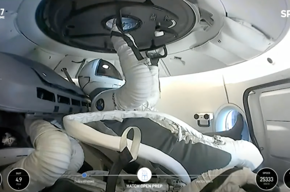 An astronaut in a space suit opens a hatch inside a spacecraft.
