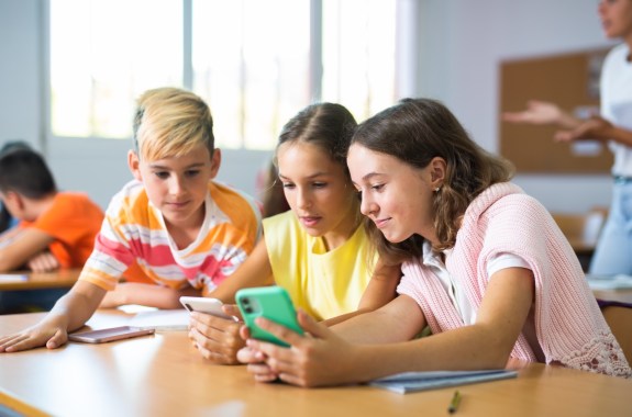 Group of kids using smartphones during lesson in school. Girls and boys using gadgets while studying.