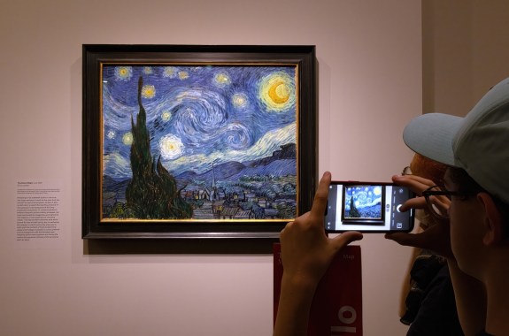 A person taking a photo of The Starry Night using their smartphone.
