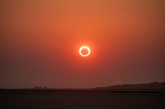 An orange sky with the moon covering the center of the sun in a ring of fire eclipse