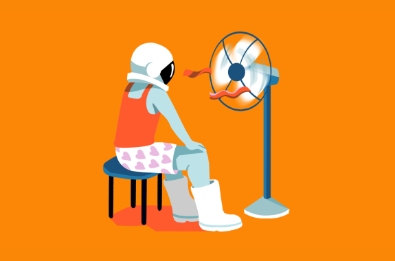 An astronaut wears their helmet, boots, and undergarments as they sit in front of a blowing fan.