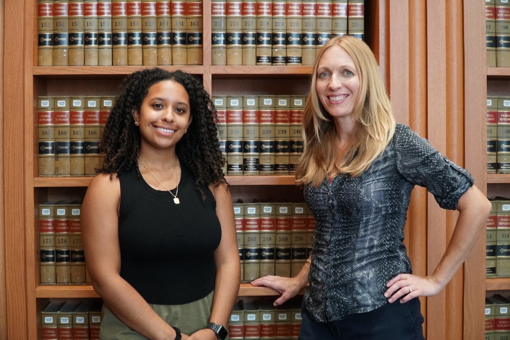 Two women stand in front of a wall of books.