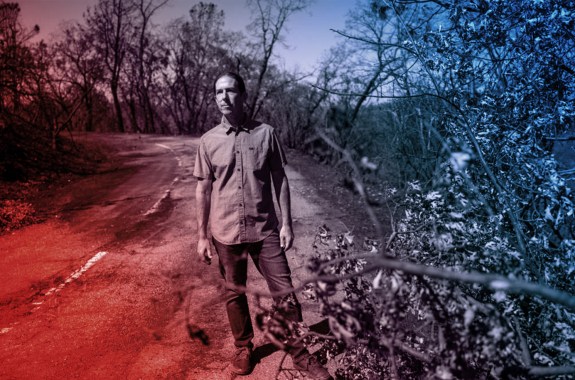 A man standing on the side of a road, surrounded by burnt trees.