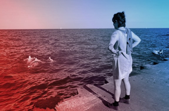 A person stands on a dock watching friends swim around in Lake Michigan.