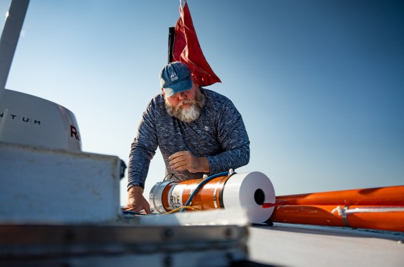 A man on a ship holding a cylinder with the word "rye" on it