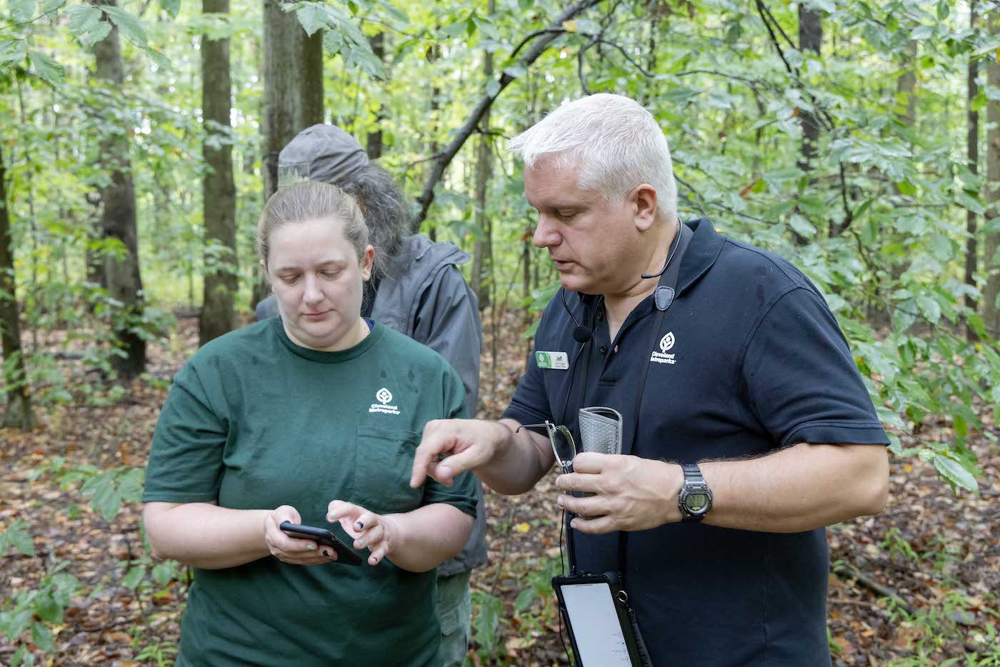 Two people stand in a forest, looking at a mobile device