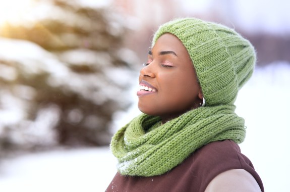 Portrait of beautiful happy woman enjoying good cold frosty sunny day at winter snow park with eyes closed, breathing deeply deep fresh air smiling