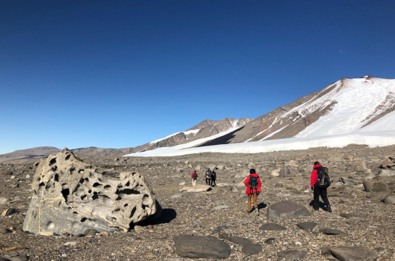 Expeditioners walking in Antarctica with a big boulder full of holes in the foreground