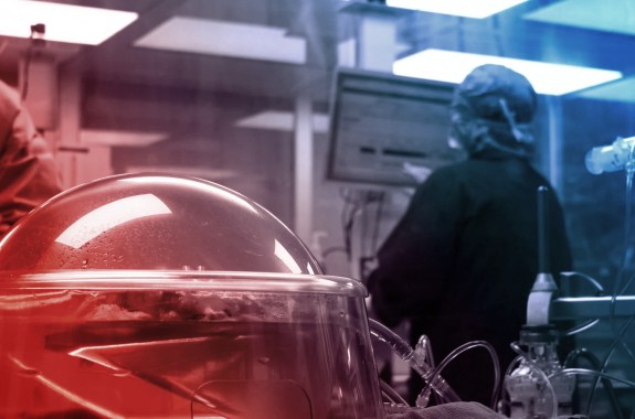 A person in PPE enters information into a computer. In the foreground, an organ rests inside a machine.