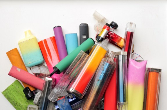 A vibrant collection of discarded electronic cigarette vapes and internal components shot over a white plastic background.
