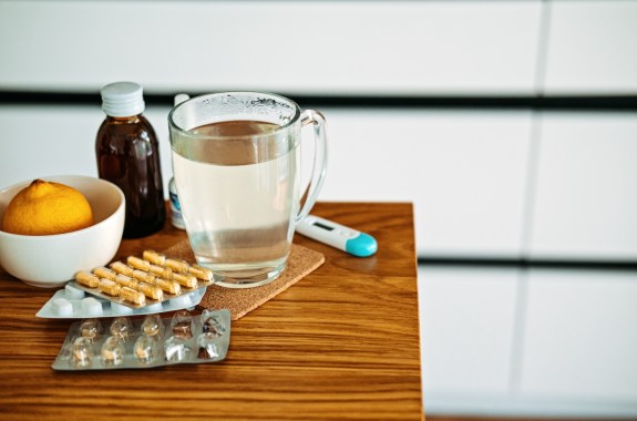 Natural and medical cold and flu remedies on table at home. Cold and flu influenza fall autumn and winter season. Cup with hot tea, lemon, thermometer pills and capsules
