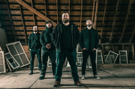 Four men stand tall in a dusty large attic