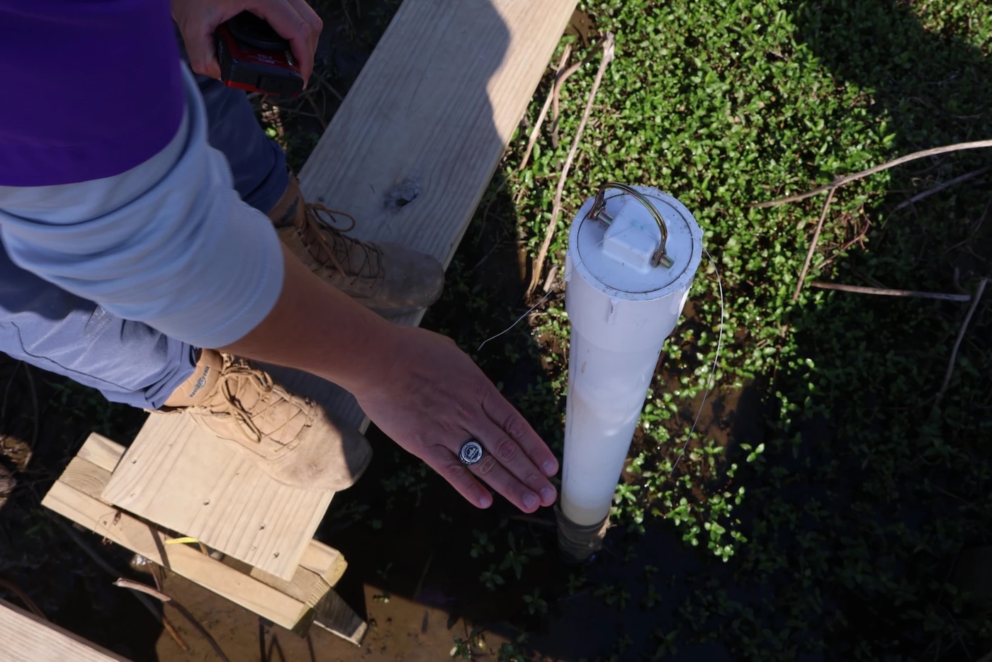 Someone holding their hand up to a PVC pipe sticking out of the ground