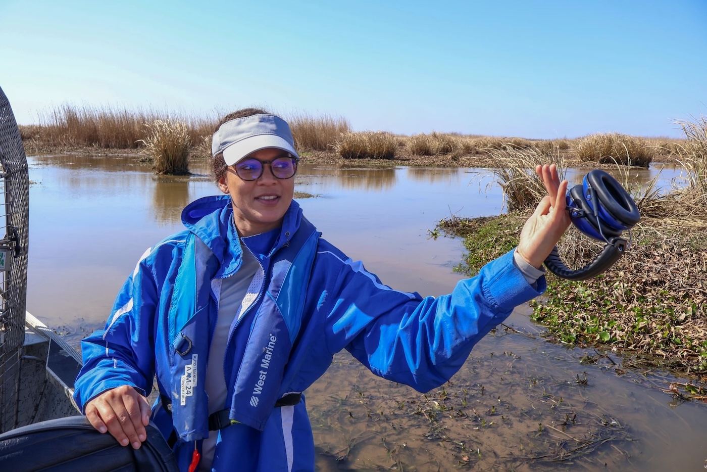 A woman holding headphones over a wetland