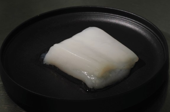 A small cube of white-colored meat on a black plate