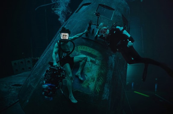Two men underwater in diving suits resting on a set of a sunken submarine