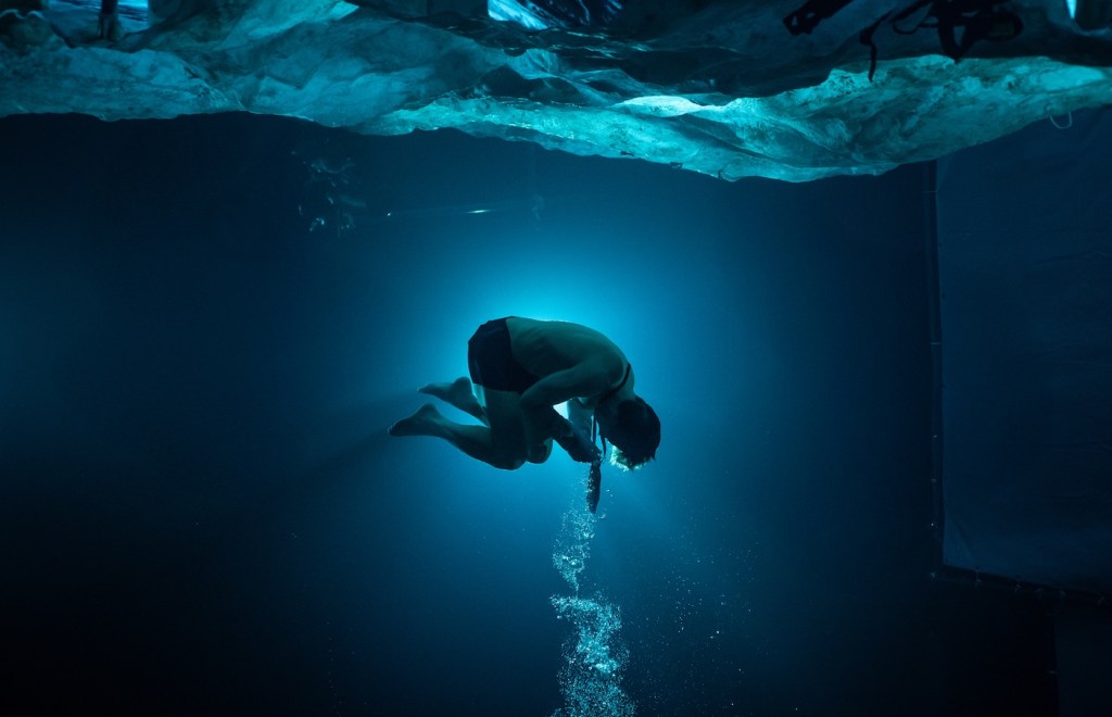A man in a swimsuit curled up while floating in water