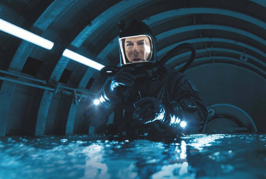 Actor Tom Cruise looking perplexed while in a diving suit in a small space flooded with water.