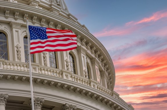 View of the United States Capitol Rotunda Dome in Washington DC with the Star Spangled American Flag against colorful dramatic sunset sky background
