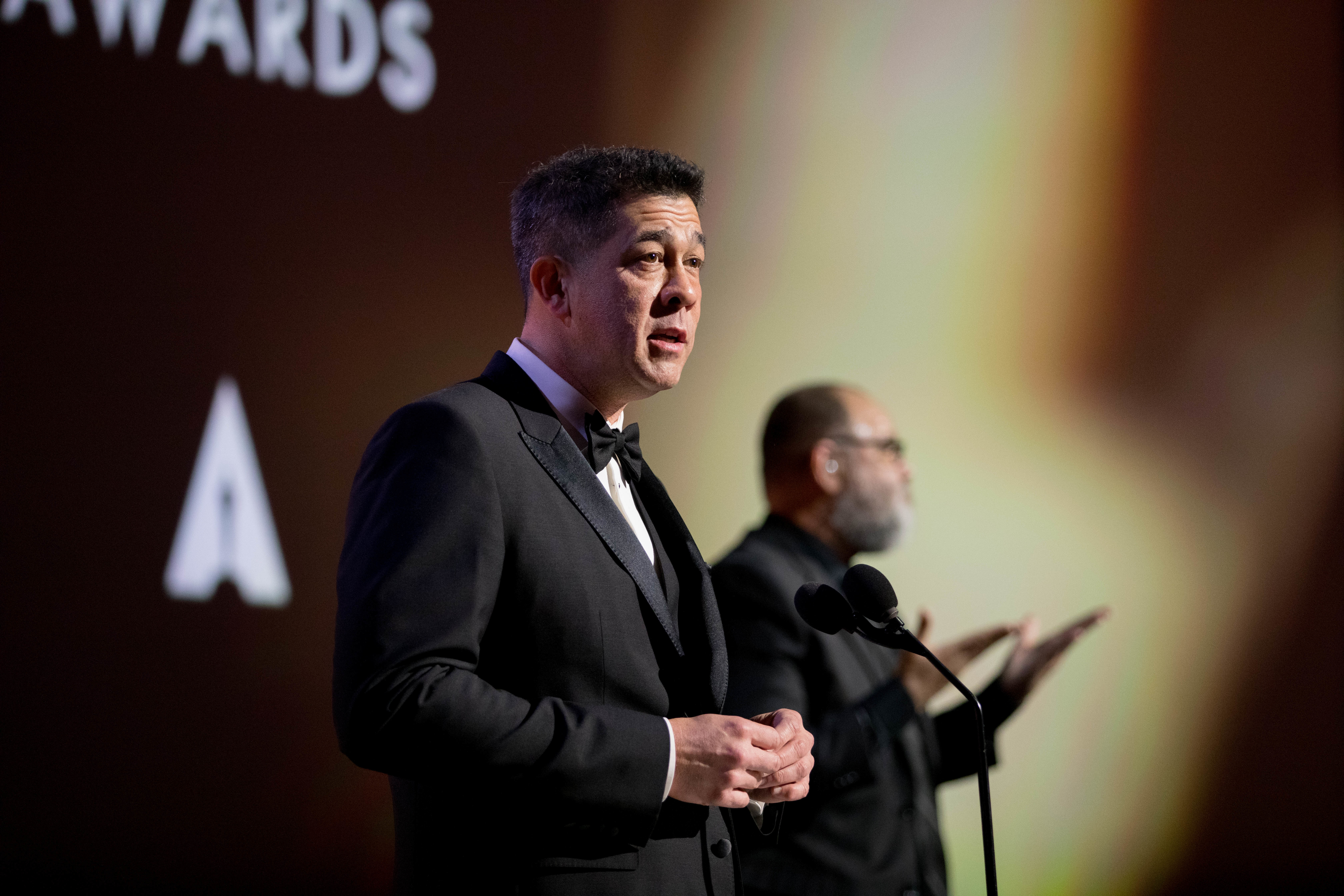 A man speaking during a ceremony in black tie attire