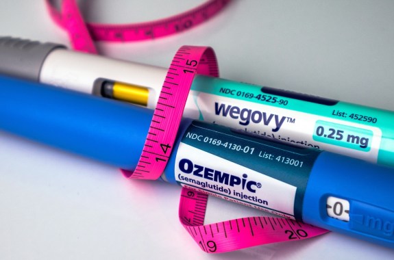 Ozempic and Wegovy pens wrapped in a pink tape measure on white background
