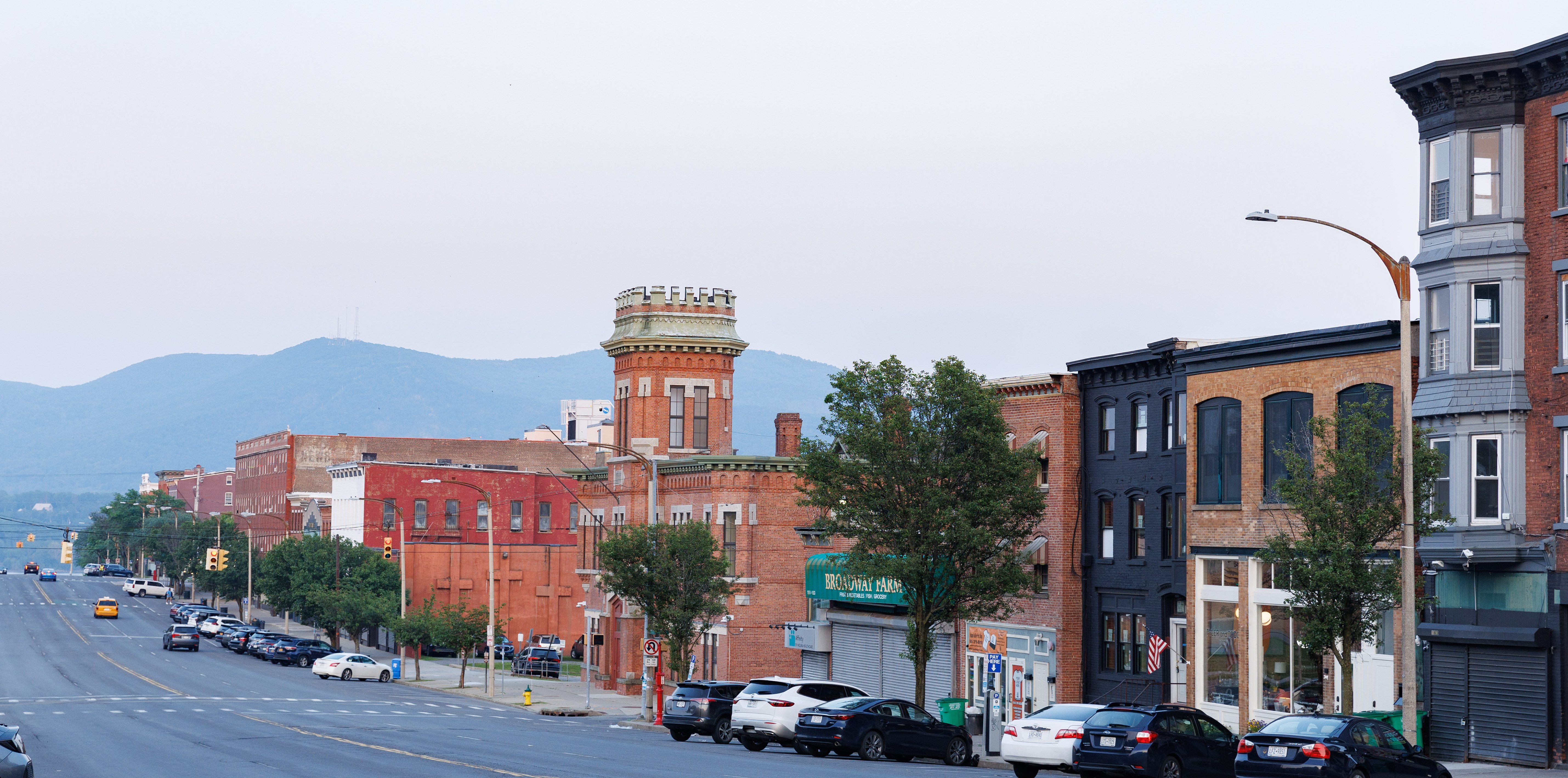 A broad street lined by brick apartment buildings and businesses, with low mountains in the background.