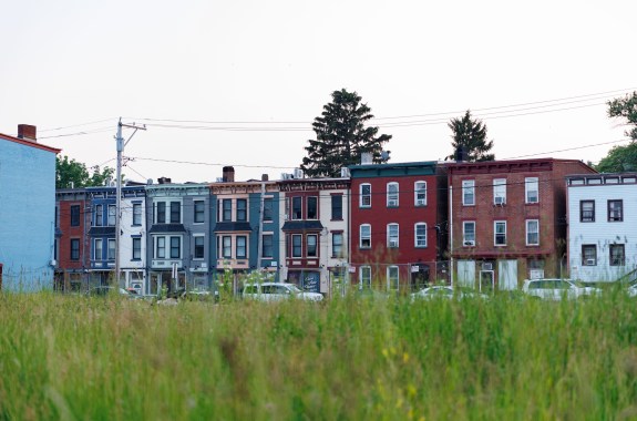 Looking across a grass field at a row of attached, multicolor, 3-story apartment buildings.