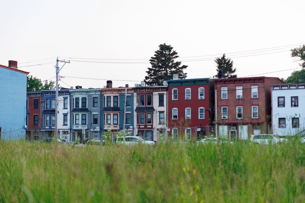 Looking across a grass field at a row of attached, multicolor, 3-story apartment buildings.