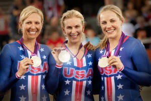 Three women in blue uniforms smile at the camera while holding up their silver medals.