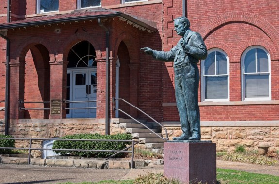 A statue of a man pointing his finger in front of a red brick building