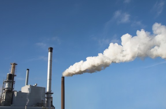 white smoke blows out of a tall industrial chimney against a blue sky